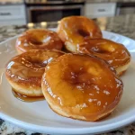 ['Close-up view of a shiny maple glaze in a bowl, with ingredients around it.', 'Side angle of a glossy maple glaze dripping from a spoon, featuring recipe ingredients nearby.', 'Detailed shot of a creamy maple glaze highlighted by a sprinkle of cinnamon on top.', 'Overhead view of a small bowl of maple glaze with confectioners’ sugar and butter scattered around.']