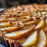 ['A close-up side view of a pear tart with thinly sliced Anjou pears on top.', 'Juicy pear tart featuring a golden crust and almond flour base, garnished with sliced almonds.', 'Side view of a freshly baked pear tart, showing the delicious caramelized pears.', 'Detailed shot of a wholesome pear tart made with natural sweeteners and almond flour.']