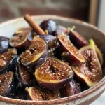 ['Close-up of a bowl filled with fresh fig compote, showcasing juicy figs and spices.', 'Side view of fig compote with whole figs, glistening with syrup, in a white bowl.', 'Detailed image of homemade fig compote, highlighting the chunks of figs and a cinnamon stick.', 'Rich, glossy fig compote in a serving dish, with fresh ingredients displayed around it.']