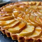 ['Close-up side view of a golden-brown French apple tart with a glossy finish and baked apple slices.', 'Side view of a freshly baked French apple tart showcasing juicy apple filling and a flaky crust.', 'Delicious French apple tart with visible apple slices and a rich, golden crust in a close-up perspective.', 'Side view of a homemade French apple tart, highlighting its flaky layers and caramelized apple tops.']
