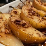 ['Close-up view of baked pears topped with crushed walnuts and cinnamon.', 'Sliced baked pears drizzled with maple syrup and sprinkled with cinnamon.', 'Juicy, caramelized baked pears arranged on a plate, highlighting texture and toppings.', 'A side view of golden-brown baked pears with a glossy finish and nut garnish.']