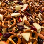 ['Close-up view of homemade apple chip trail mix featuring apple slices, pretzels, almonds, cranberries, seeds, and colorful chocolates.', 'Side view of a bowl filled with homemade apple chip trail mix, showcasing various ingredients like pretzels and dried fruits.', 'Detailed shot of a homemade apple chip trail mix with vibrant colors from candied chocolates and nuts against a textured background.', 'Fresh homemade apple chip trail mix displayed in a bowl, highlighting the mix of apples, nuts, and snacks.']