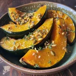 ['Close-up of roasted kabocha squash wedges garnished with thyme and garlic.', 'Side view of caramelized kabocha squash slices topped with fresh thyme and garlic.', 'Juicy kabocha squash wedges drizzled with olive oil and sprinkled with herbs.', 'Golden roasted kabocha squash with thyme and garlic on a rustic plate.']