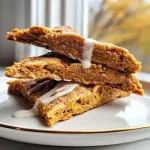 ['Close-up view of golden-brown low carb pumpkin spice scones with a spiced topping.', 'Side angle shot of fluffy pumpkin spice scones, showcasing their texture and rich color.', 'Delicious stack of gluten-free pumpkin spice scones with a glossy glaze.', 'Close-up detail of moist low carb scones featuring pumpkin and spice elements.']