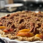['Close-up view of Peach Maple Pecan Crumble with a golden brown crust and juicy peach slices.', 'Side angle of a delicious Peach Maple Pecan Crumble, highlighting its crumbly topping and fruit filling.', 'Rich Peach Maple Pecan Crumble displayed on a plate, showing the layered texture of peaches and pecans.', 'Lush, baked Peach Maple Pecan Crumble with a crispy top and visible pieces of peach and pecan.']