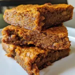 ['Close-up of golden-brown Pumpkin Spice Bars with a moist texture.', 'Side view of delicious Pumpkin Spice Bars topped with chopped nuts.', 'Homemade Pumpkin Spice Bars on a plate, showcasing their spiced layers.', 'A slice of Pumpkin Spice Bars, highlighting the warm spices within.']