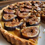 ['Close-up view of a spiced fig and walnut tart with a golden crust, garnished with orange zest.', 'Side angle of a freshly baked spiced fig and walnut tart, showcasing figs and walnuts on top.', 'Detailed shot of a slice of spiced fig and walnut tart, highlighting its rich filling and crumbly crust.', 'Artistic close-up of a fig tart with visible orange zest and chopped walnuts, emphasizing texture.']