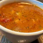 ['Close-up view of a bowl of spicy apple soup with a garnish.', 'Side view of a creamy, vibrant spicy apple soup in a rustic bowl.', 'Close-up of a spoonful of spicy apple soup showcasing its texture.', 'Detailed look at a bowl of spicy apple soup with visible apple chunks.']
