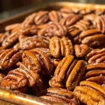 ['Close-up view of toasted pecans on a wooden surface.', 'Side view of crispy, golden-brown toasted pecans in a bowl.', 'A collection of freshly toasted pecans with a glossy finish.', 'Detailed shot of pecans showing texture after being toasted.']